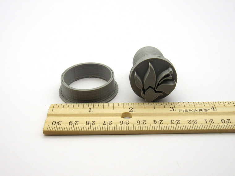 An abstract flower with stamen round pendant clay stamp with cutter. Next to ruler. Measuring approximately 1 inch wide.