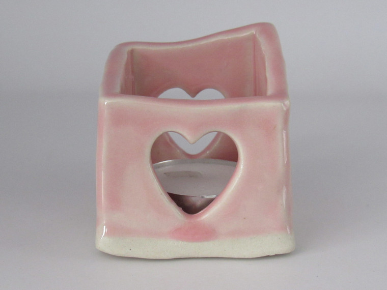 A handcrafted ceramic pottery Pink Tea Light Votive Candle Holder. The candle holder is uneven around the top, in an abstract pattern. There is a tea light candle inside the candle holder.