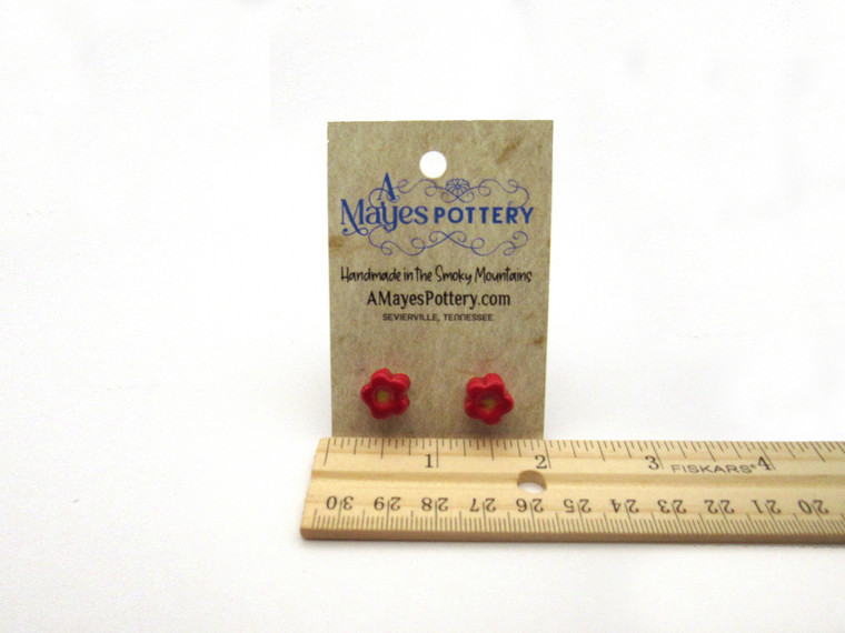 A set of handcrafted ceramic small red flowers with yellow centers stud post earrings. With ruler. On an A Mayes Pottery card.