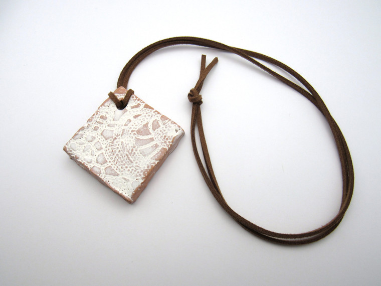 An aromatherapy terracotta diamond shaped white lace ceramic handmade necklace. On a brown cord necklace.