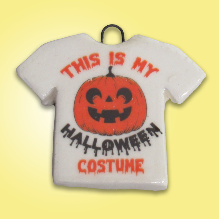 A handmade ceramic Halloween Tshirt pendant saying "This is my Halloween Costume"  with a smiling jackolantern in the middle. On a yellow background.