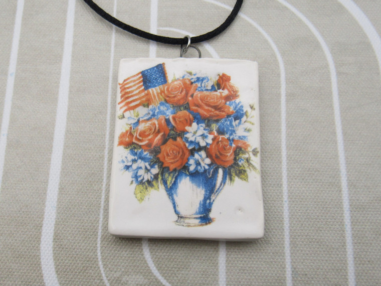 A Patriotic Flowers in Vase with Flag Infusion ceramic rectangle pendant on a black cord necklace. With a beige and white background.