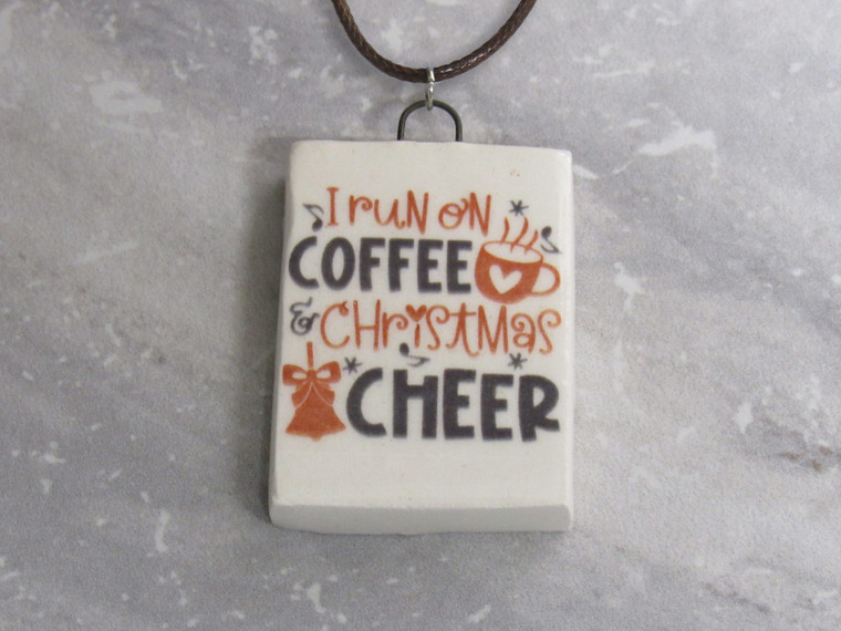 Fun Christmas Handmade Ceramic Necklace with the words "I run on Coffee and Christmas Cheer". On a black cord necklace.  With a gray marble look background.