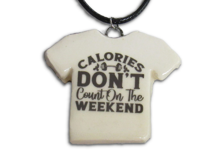 A handmade ceramic Tshirt pendant necklace with the words "Calories don't count on the weekend." On a black cord necklace.