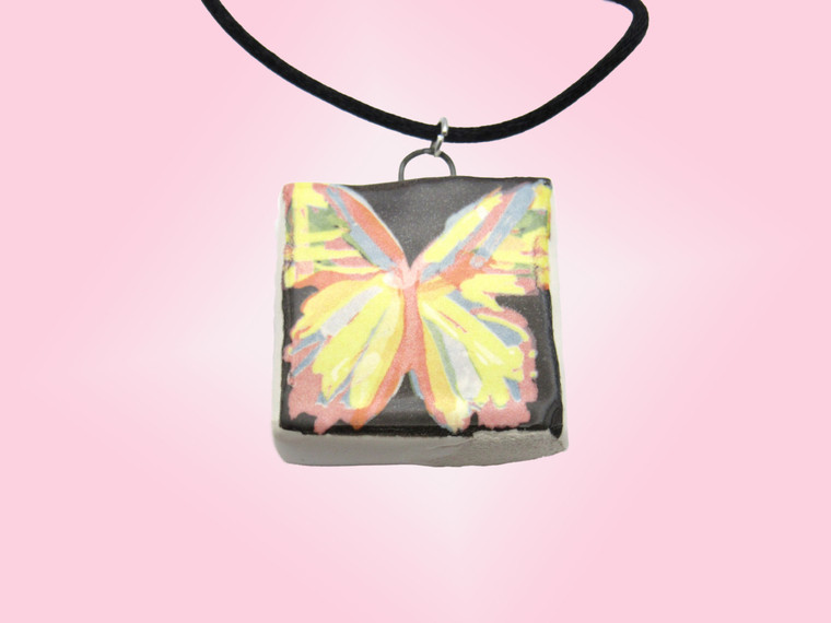 A handmade abstract colorful butterfly square jewelry pendant. On a black cord necklace. With a pink background.