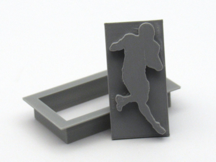 A running football player rectangular pendant clay stamp with cutter. Shown with stamp tilted on top of cutter. A running football player rectangle pendant clay stamp with cutter. Shown with stamp tilted on top of cutter.