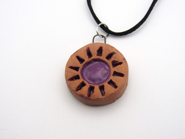 A handmade Abstract Sun Terracotta Pendant Necklace. The sun and sun rays are painted purple. With a black cord necklace. Made in America.
