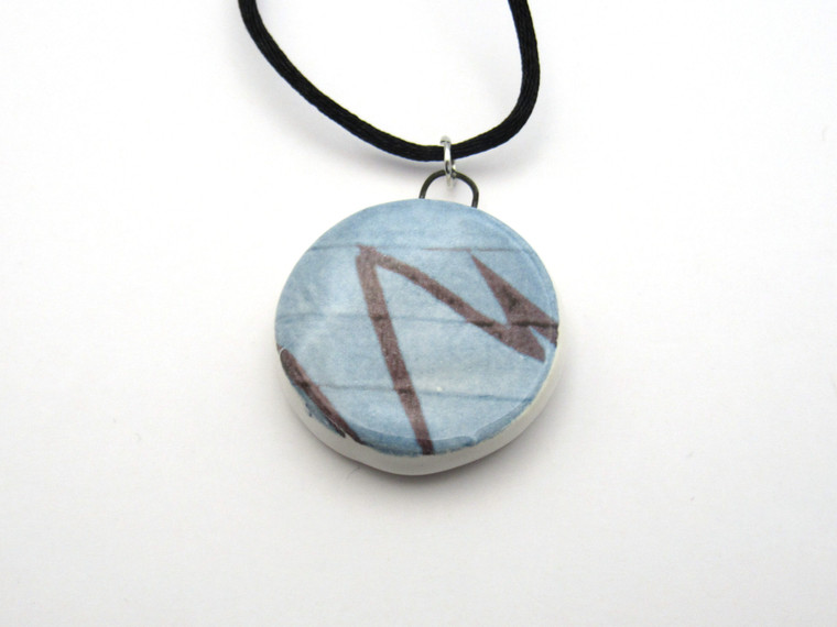 A round Blue & Black Abstract Design Ceramic Pendant Necklace. On a black corded necklace.