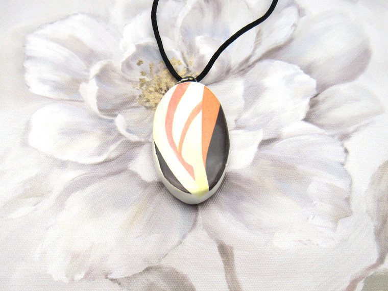 An oval Colorful Abstract (Design 2) Ceramic Pendant necklace. With black corded necklace. Shown on a white floral look background.