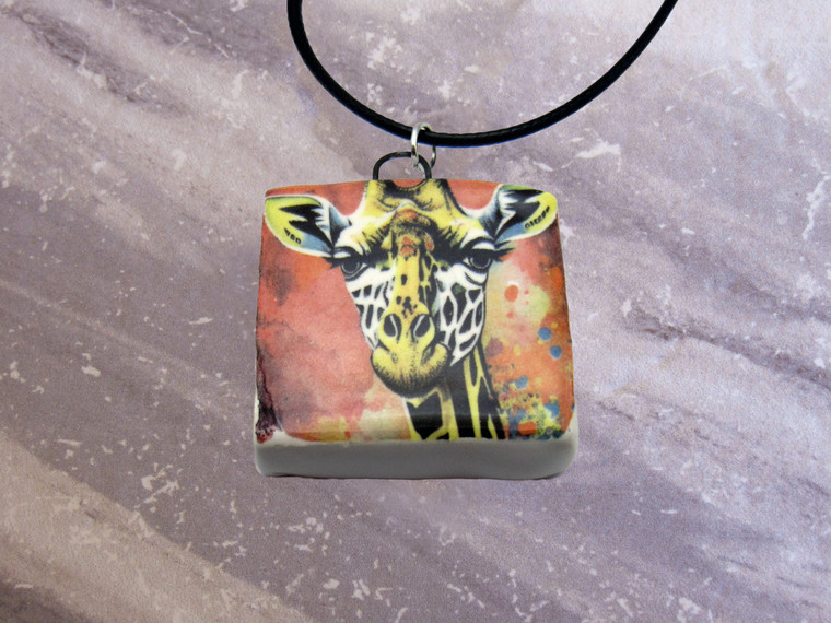An Abstract Giraffe Handmade Ceramic Necklace. On a black corded necklace. With a gray marble look background. An abstract giraffe handmade ceramic necklace. On a black cord necklace.