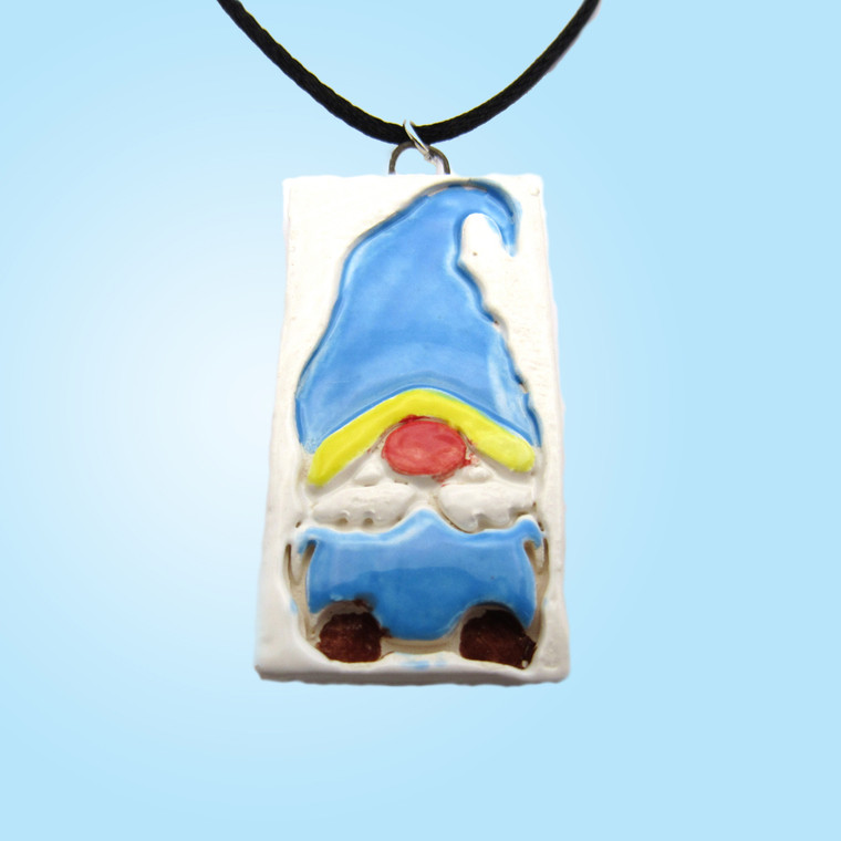 A blue background with a Handmade ceramic cute and colorful Gnome pendant necklace. On black corded necklace.
