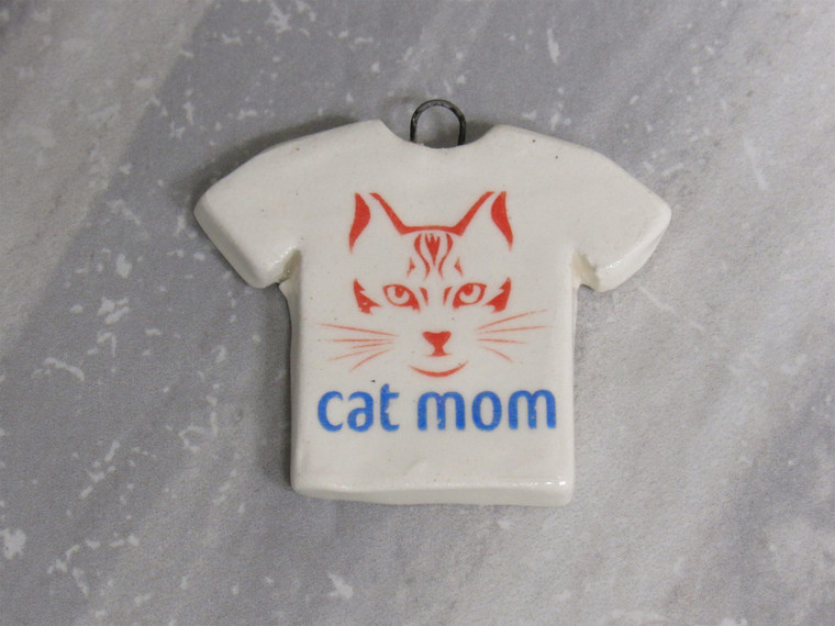 A Handmade Ceramic Tshirt Necklace pendant featuring "Cat Mom" and stylized cat face. On a gray marble look background. A handmade ceramic Tshirt Necklace pendant featuring "cat mom" and stylized cat face. On a gray marble look background.