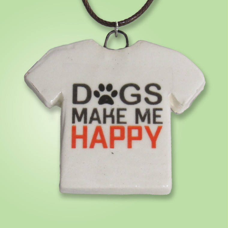 A green background with a Handmade Ceramic Tshirt Necklace saying "Dogs Make Me Happy". On a black corded necklace. A green background with a handmade ceramic Tshirt necklace saying "Dogs Make Me Happy". On a clack cord necklace.