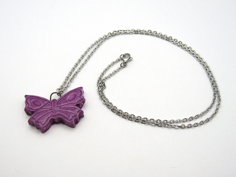 A Purple Ceramic Butterfly Pendant Necklace Handmade from fired earthenware clay. On a silver colored chain necklace. A purple ceramic butterfly pendant necklace. Handmade from fired earthenware clay. On a silver colored chain necklace.