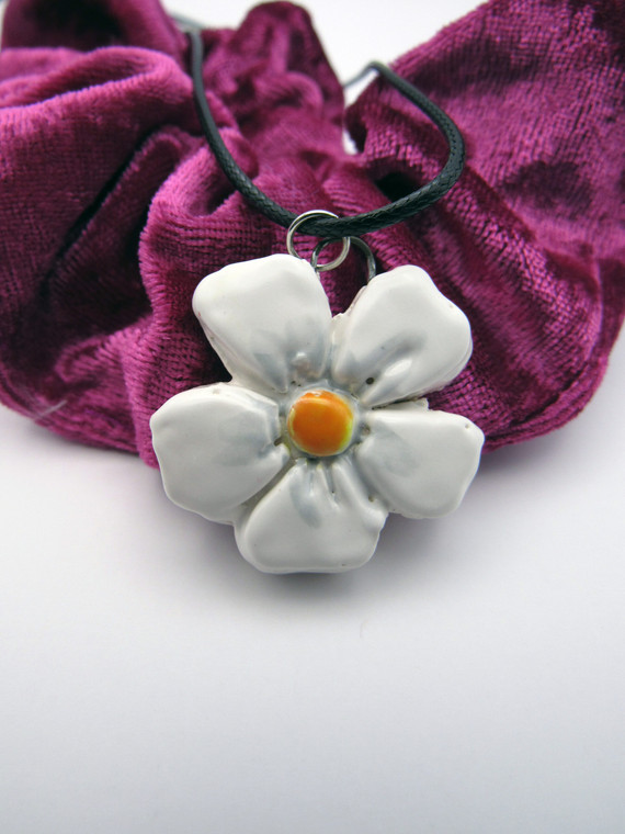 A 5 Petal shaped Ceramic Flower handcrafted necklace. With white petals and an orange center. On a black corded necklace. Shown on Burgundy material.