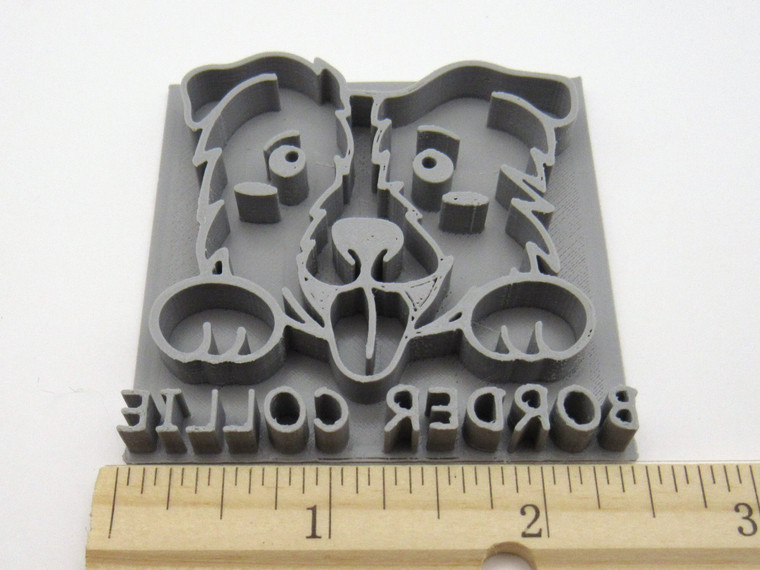 A Border Collie mug clay pottery stamp. With a Border Collie head with paws on top of the word Border Collie. With ruler. Showing approximately 2.5 inches wide.