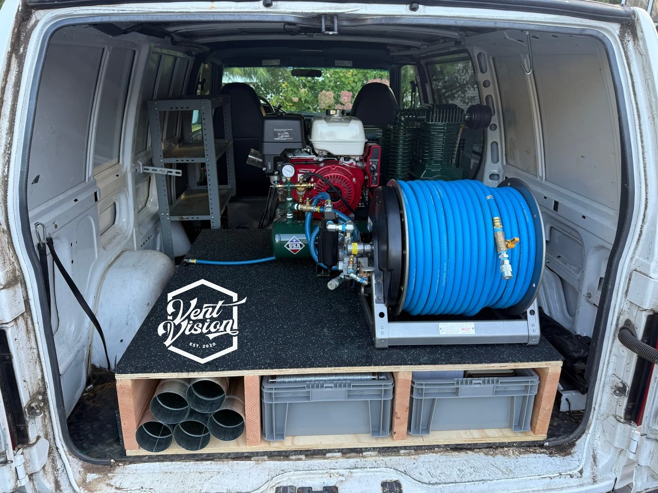DIY plywood storage platform with two bins and a side cubby beneath a compressor and hose reel in a service van