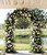 wedding arch decorated with plants and flowers in front of a body of water