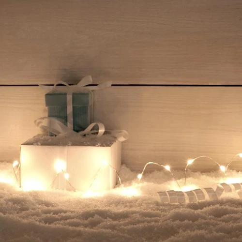 6 Ft Fairy Wire, 36 Warm White LEDs, Power Option: Waterproof AA Battery Pack with Remote, illuminated in a cozy winter setting with snow and gift boxes.