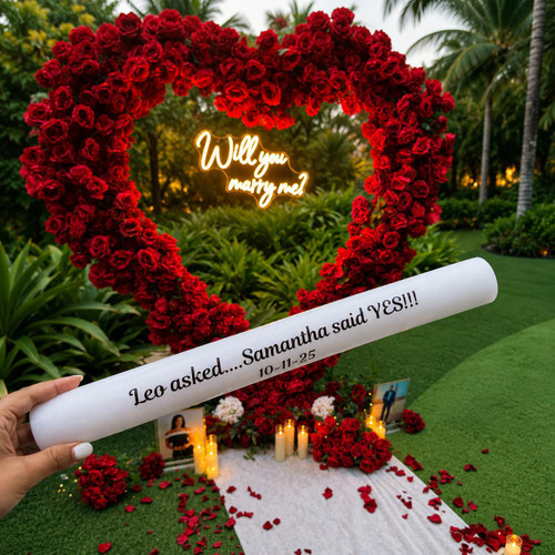 Customized 7 Mode LED Foam Glow Sticks | Flashing Foam Sticks - Extreme Glow, a white foam stick with personalized text for a marriage proposal in an outdoor garden setting with a heart-shaped flower arrangement and romantic decor.