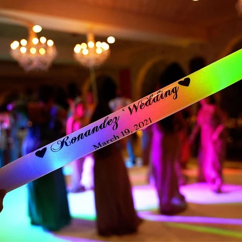 Rainbow 4 Color Flashing Foam Stick, illuminated at a party with a wedding inscription and date, held against a background of dancing guests and colorful lighting.