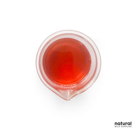 A small beaker filled with red to reddish-brown viscous liquid, representing Tocopherol T-50 (Vitamin E). The liquid has a glossy surface, and the beaker is placed on a white background. The "Natural Bulk Supplies" logo is visible in the lower right corner.