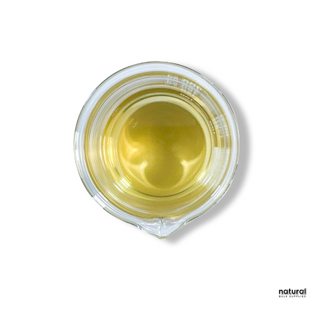 A top-down view of a clear glass container filled with a translucent, light golden liquid. The liquid has a smooth surface, reflecting light slightly. The container is placed against a white background with a subtle shadow on one side. The "Natural Bulk Supplies" watermark is visible in the lower-right corner. A top-down view of a clear glass container filled with a translucent, light golden liquid. The liquid has a smooth surface, reflecting light slightly. The container is placed against a white background with a subtle shadow on one side. The "Natural Bulk Supplies" watermark is visible in the lower-right corner.