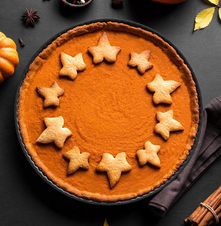 A pie on a black surface , pie is in orange in color. Few spices like cinnamon in the flat overlay