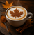 A warm maple latte in a white cup topped with cinnamon in the shape of a maple leaf, surrounded by cinnamon sticks and autumn leaves.