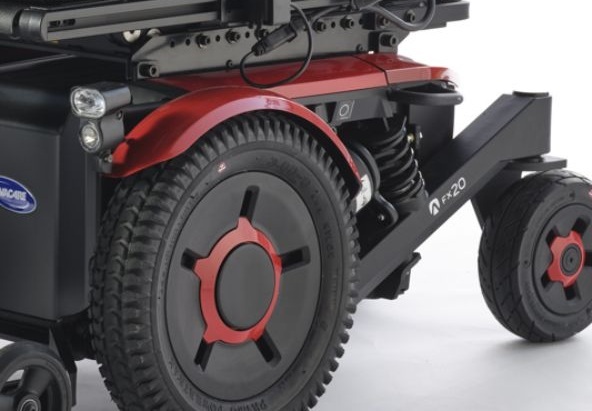 Close-up of Invacare Aviva FX20 power wheelchair front-wheel drive system with red accent hub and suspension for enhanced mobility.