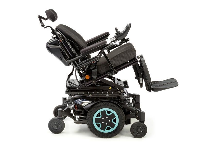 Invacare TDX SP2 HD power wheelchair in a reclined position, featuring a black frame with teal wheel accents, padded seat, backrest, headrest, and adjustable armrests and footrests, designed for heavy-duty use and advanced positioning