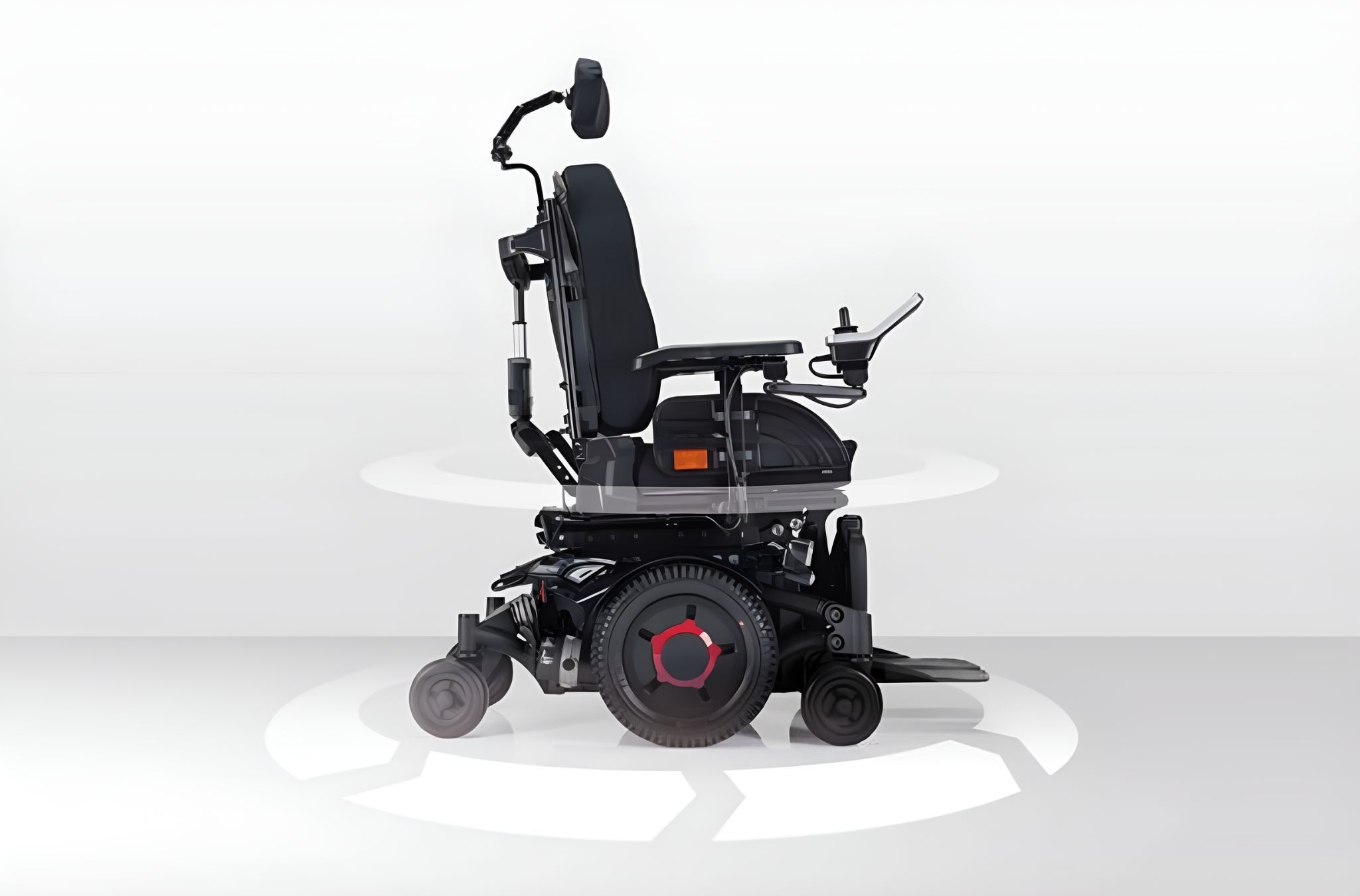 A motorized wheelchair with a black seat, headrest, and joystick control on the right armrest. The base features large wheels with red accents and smaller front wheels, set against a light gray background with circular graphics suggesting motion.