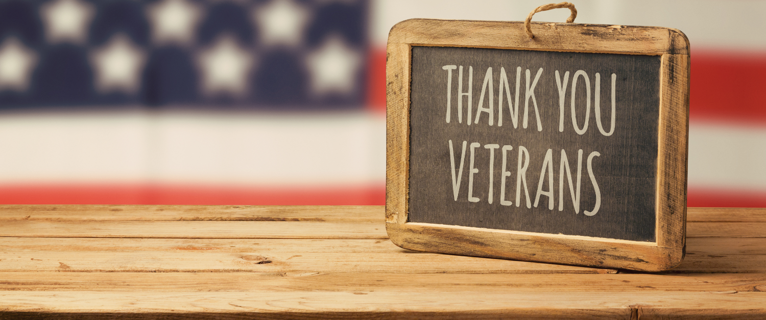 Wooden chalk board on a wooden table reads "Thank You Veterans" with an American Flag in the background