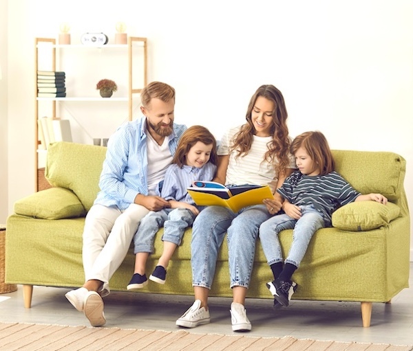 A family of four sitting together on a sofa reading a book together stimulating their minds.