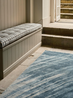 David Rockwell Splash Sea Runner, blue brushstrokes on ivory, laid on flagstones beside a cushioned bench