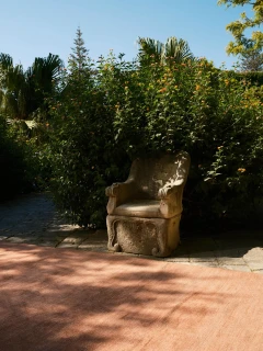 Vara rug in Clay, outdoor editorial shot with a weathered stone garden chair