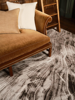 David Rockwell Falls Graphite rug, close view of flowing charcoal and silver striations beneath an ochre velvet sofa