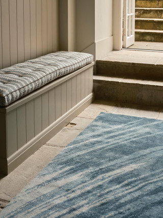 David Rockwell Splash Sea Runner, blue brushstrokes on ivory, laid on flagstones beside a cushioned bench