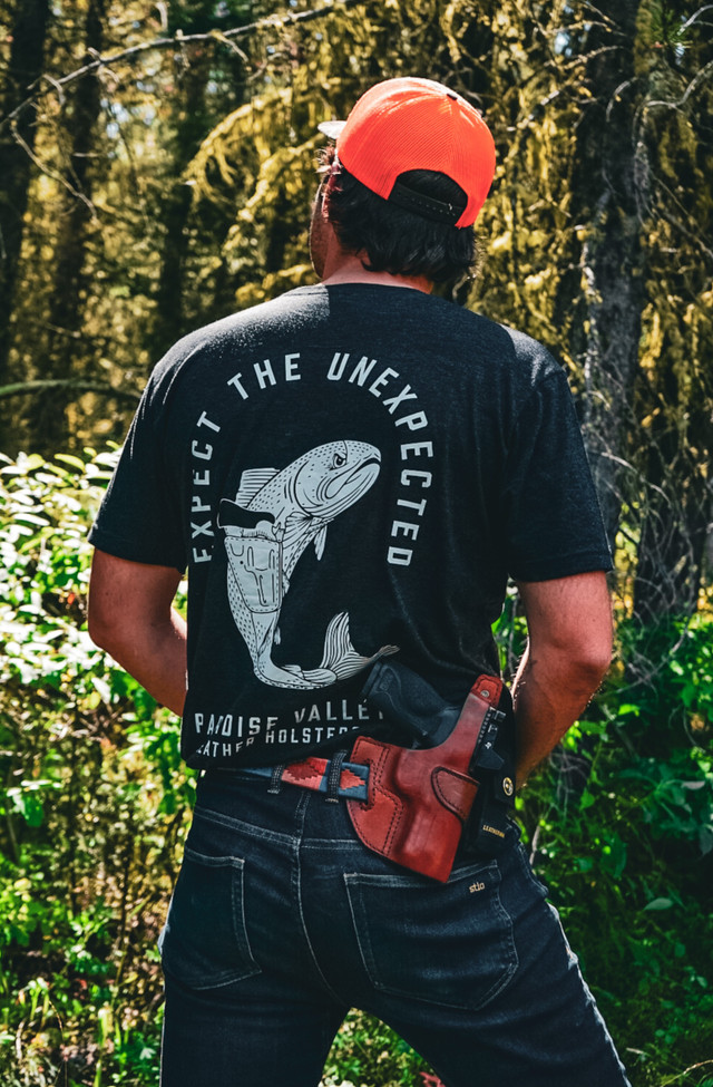 Paradise Valley Leather customer in the woods wearing an Expect the Unexpected shirt and a leather holster