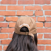 back of Theo Chocolate Hat with bill in chocolate color on model in front of brick wall