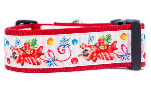 A red dog collar with a design includes a red airplane carrying presents, snowflakes, candy canes, and colorful ornaments.