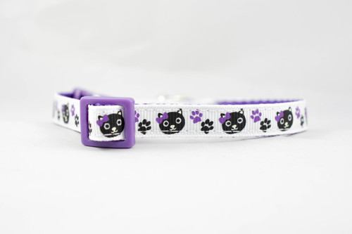 A white cat collar with a purple adjustable safety buckle and purple nylon. The collar has a repeating pattern of black cats with purple bows and purple paw prints.