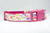 A pink dog collar with a white background and a floral pattern featuring leaves and flowers.