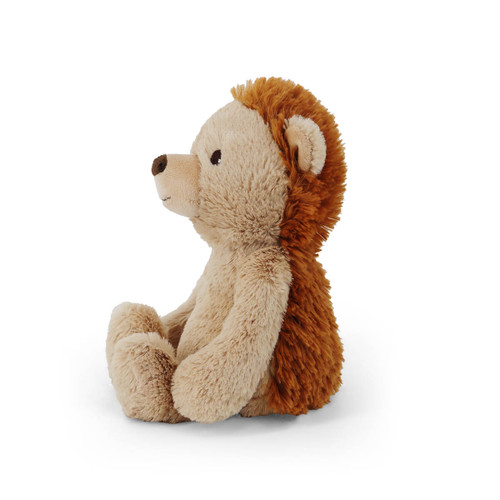 A soft, plush toy shaped like a hedgehog. The hedgehog is sitting in a three-quarter profile, looking to the left. Its fuzzy, dark brown "spikes" are visible along its back, contrasting with its light tan face and belly.