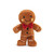 A soft, plush toy shaped like a gingerbread man. The toy has a brown body with white embroidered "icing" swirls on its arms and legs, and a red bow tie at its neck. Its face has black eyes, embroidered rosy cheeks, and a stitched smile. The toy is standing upright against a white background.
