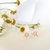 Gold stud earrings with pink pearl petals and a pavé crystal center in a daisy design, displayed beside fresh white daisies.
