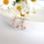 Gold hoop earrings decorated with clusters of delicate pink pearls, displayed on a white dish with daisies in the background.