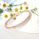 Gold daisy bangle bracelet adorned with sparkling crystal-studded floral motifs, displayed on a white surface with fresh daisies in the background.