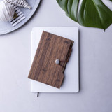 A sticky note pad with a wooden-textured cover, placed on top of a white notebook, featuring a logo.