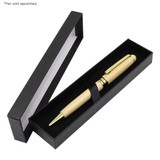 A black box with a clear lid contains a beige pen with gold accents. The pen is secured with an elastic band.